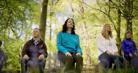 Four attendees to Xhale Mindfulness meditating in the forest.