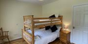 Spacious family room with bunk bed sleeps 3 Bedside cabinet with lamp and chair at bottom of bed against the wall.