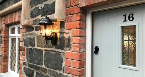 Image shows front door of No 16 with lantern on the brick wall outside