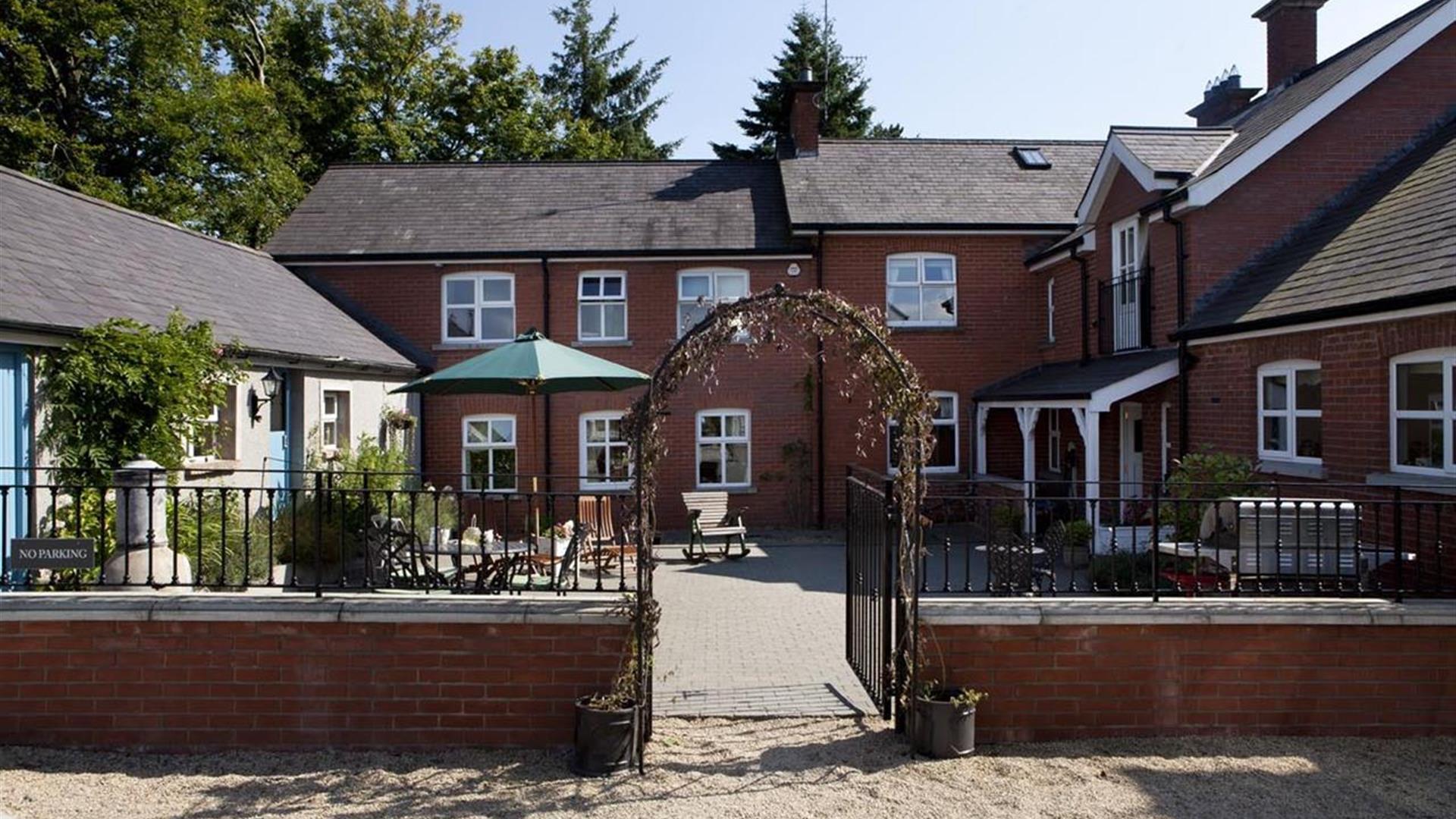Image shows front of property with archway entrance and small courtyard with seating area