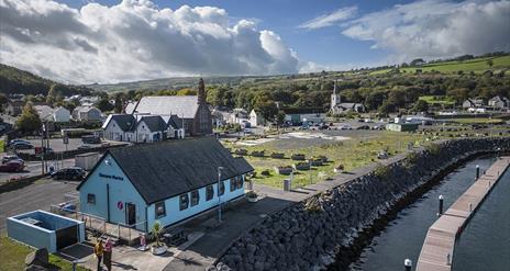 Aerial view of blue Glenarm Tourism building with town in the background and marina jetty in the foreground