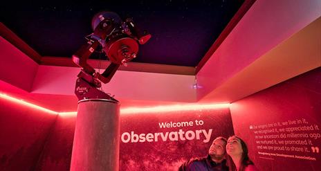 A couple looking up at a telescope at the OM Dark Sky Observatory