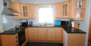 Fully equipped kitchen with electric hob and oven, dishwasher, microwave, fridge and small freezer section.