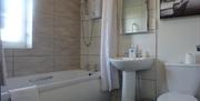 Image shows bathroom with electric shower over bath, sink with mirror above and toilet.
