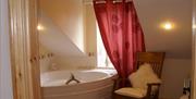 Image of a large corner bath, a red curtain and an arm chair with a fluffy cushion