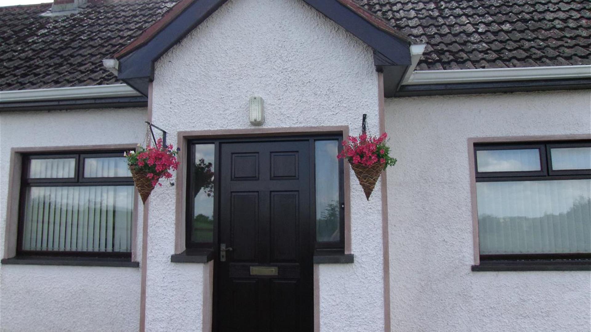 Image of the front of a white bungalow with flower baskets hanging on either side of the door