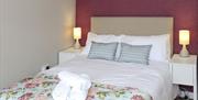 Double bed with 2 bedside lockers, floral blanket and white towels