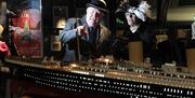 Image of a lady and gent dressed in their old fashioned finery looking at a model display of the Titanic in the exhibit