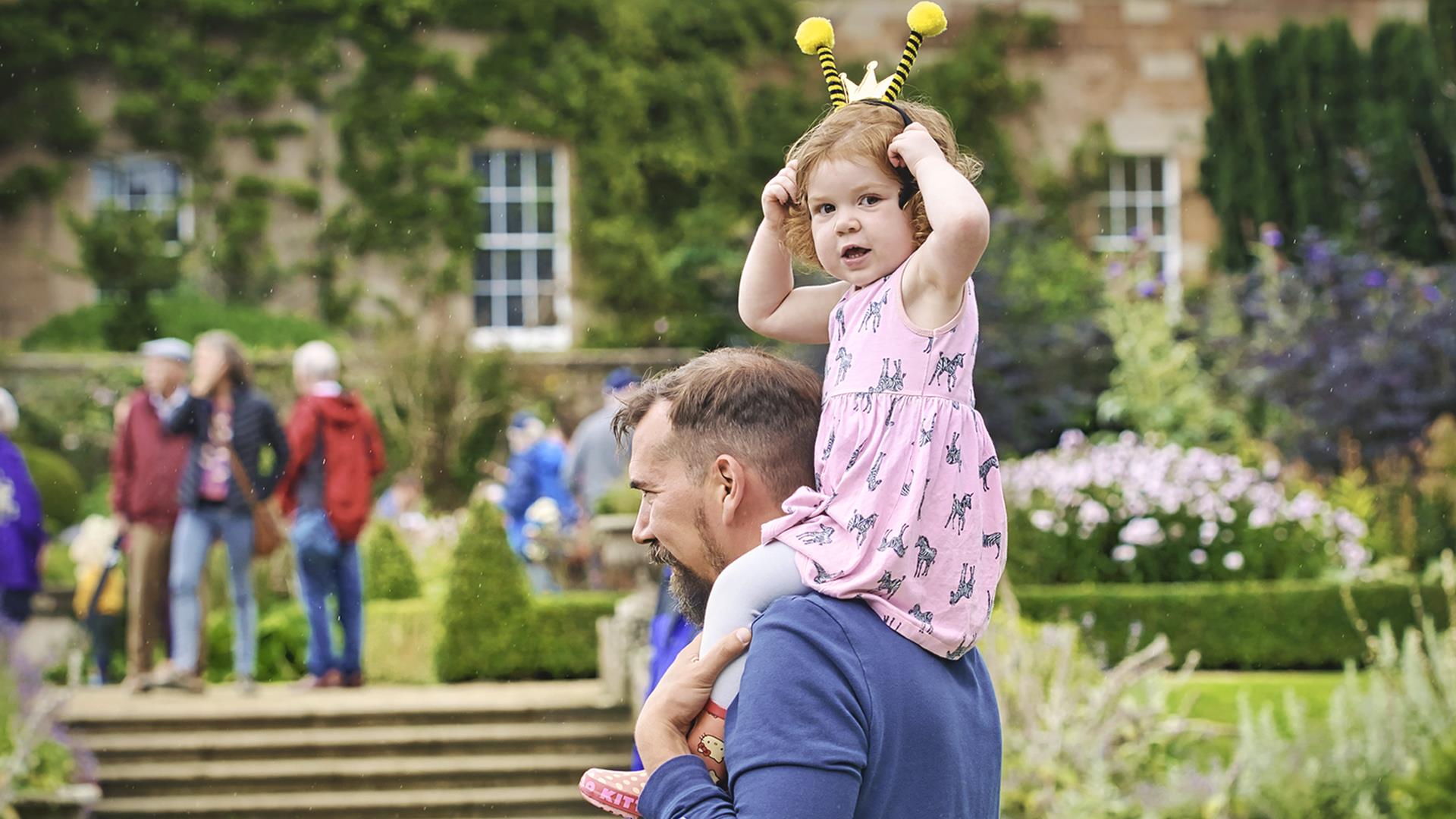 Child with a bee headband sitting on her father's shoulders in front of Hillsborough Castle