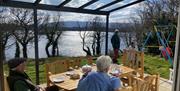 People eating outside at Shamrock Cottage, looking over the lake (Lough Erne), with a child enjoying the swing in the garden.