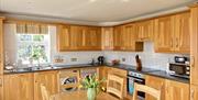 View of kitchen at Shamrock Cottage with sink, washing machine, dishwasher, tumble dryer, microwave, kettle and table with chairs for 6 guests.