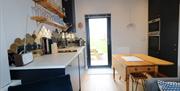 Navy kitchen, pale gray walls and worktops. Gold wall tiles. Stacking oven and micro. Wooden kitchen with two benches. Full glass back door to garden.