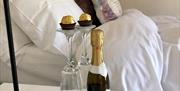 Image shows bed with chocolates and bottle of bubbly on bedside table