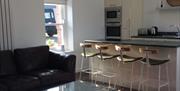 Image shows breakfast bar and 4 stools, window, oven, microwave and sink