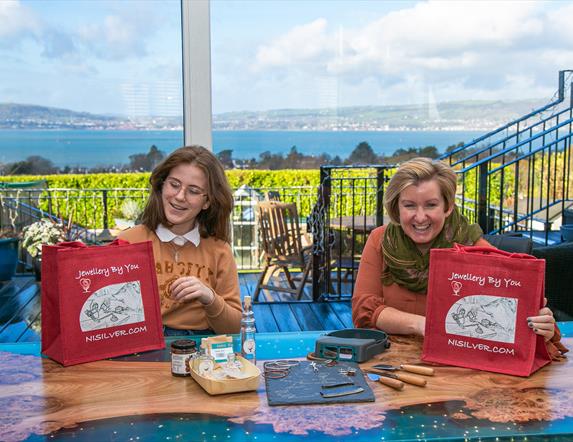 Lady and Girl Overlooking Panoramic  View of Belfast Lough from Inside House with Jewellery by You Gift Bags in Hand