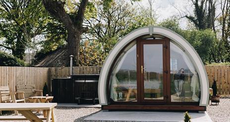 Exterior view of Glamping Pod with hot tub in background and picnic table to the front of the garden area.