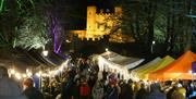 Stalls lined up along the treelined, festively lit, The Dark Walk at Royal Hillsborough Christmas Market with Hillsborough Fort in the background.