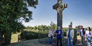 A group stand beneath a large cross, listening to Jim as part of the Poetry and Prayers experience