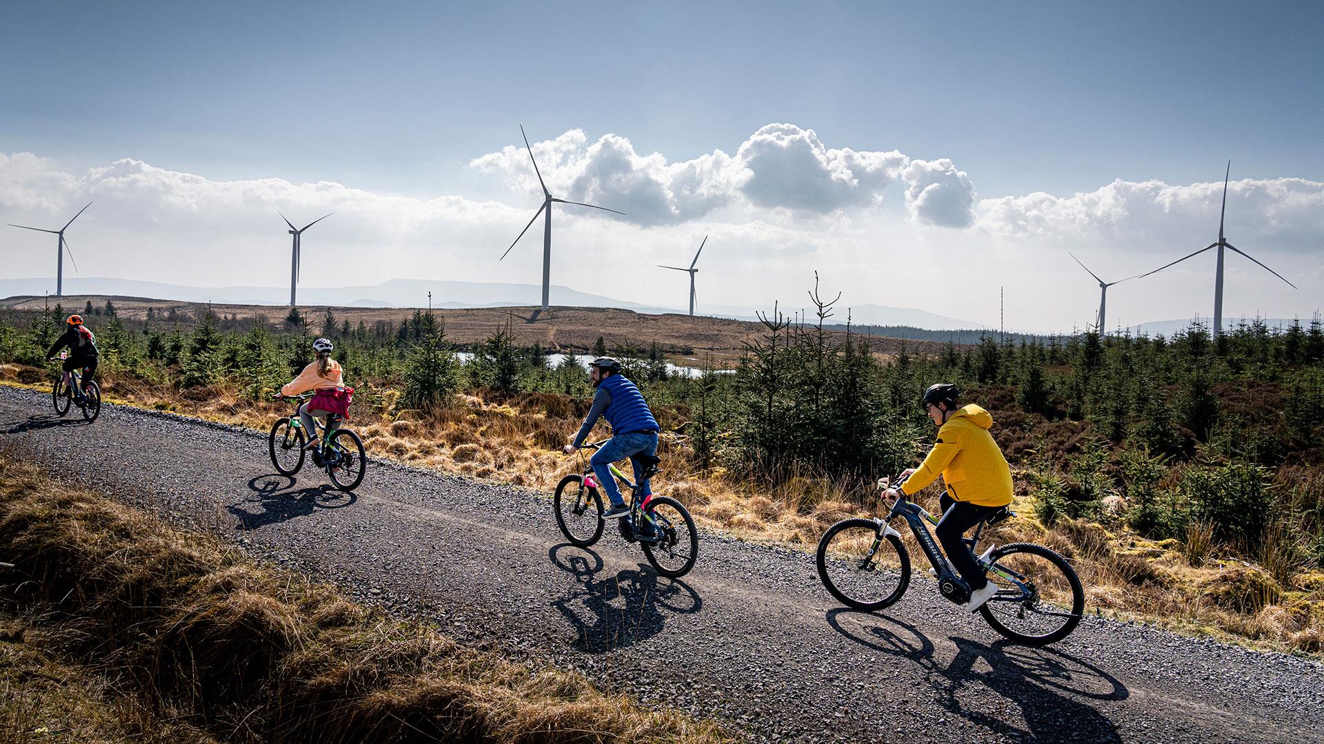Group in single file on electric bikes on a trail with wind turbines in the background enjoying the Electric Escape experience with Corralea Adventure