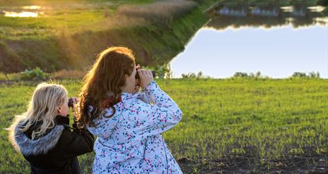 two young girls looking through binoculars over the wetlands
