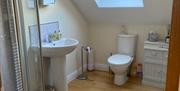Image shows en-suite bathroom with shower, wash basin and toilet, wooden floor and rug
