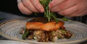 A man's hands placing green leaves on top of a piece of salmon
