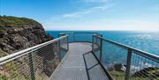 metal walk bridge overhanging the sea cliff with standing viewpoint at end overlooking the sea.
