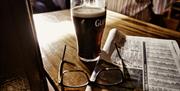 Pint of Guinness sitting on a table beside a pair of reading glasses and newspaper