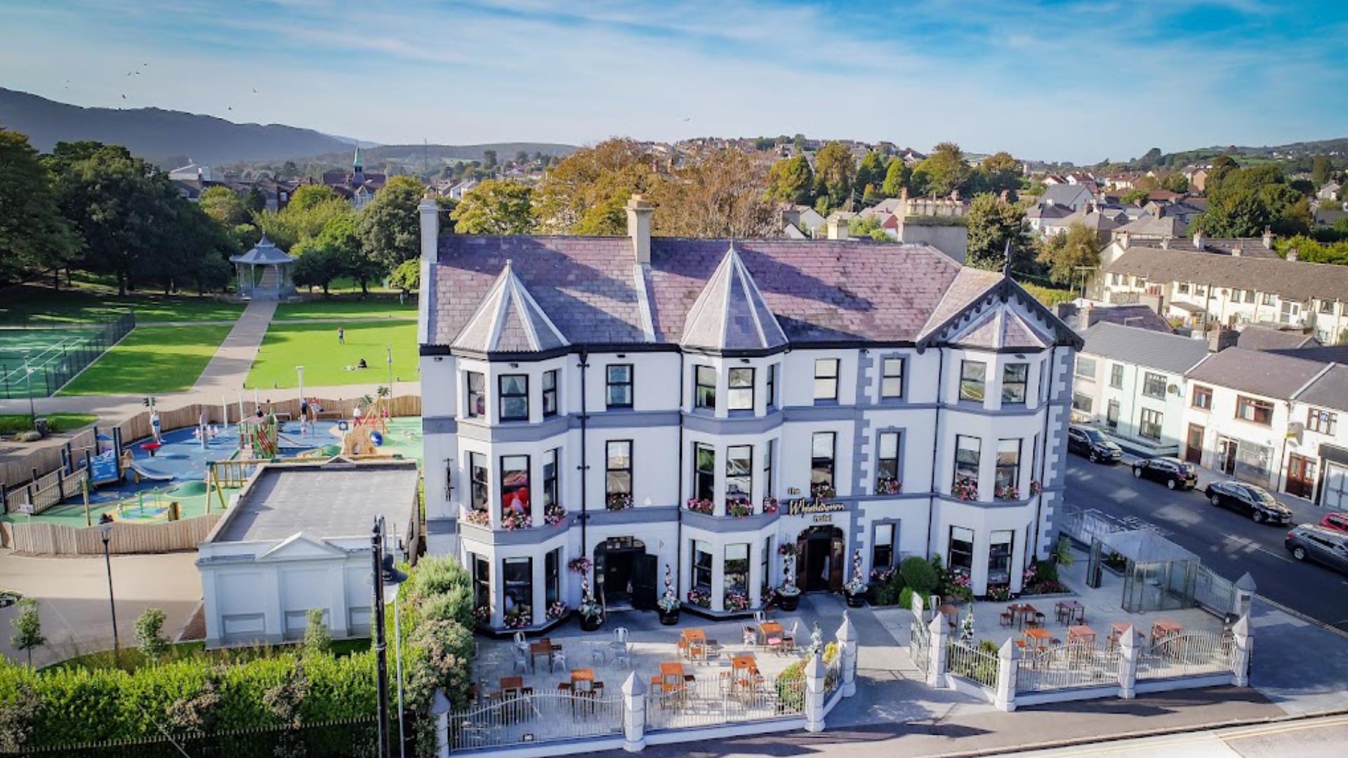 Beautiful exterior of Whistledown Hotel with blue skies, play park to the left and Warrenpoint Band Stand in the distance.