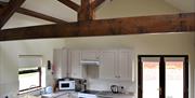Image shows a wide shot of the kitchen including the feature roof trusses and patio doors.