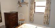 Image shows opposite corner of bedroom to previous image with window, chair and dresser.