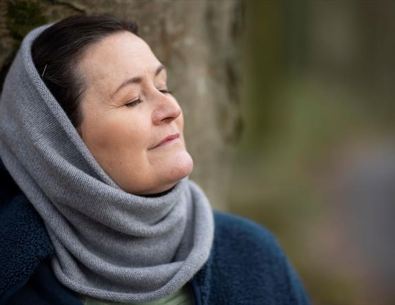 connecting to nature - image of womans head and shoulders with eyes closed. standing with back against a tree.