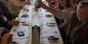 An image of a large group of people sat around a long table enjoying homemade treat