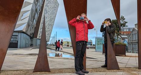 Two visitors taking pictures with Konica Pop cameras at the Titanic sign.
