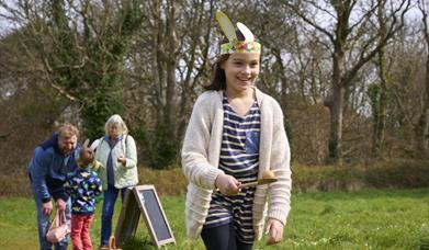 A girl balancing an egg on a spoon with family members in the background