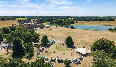 An aerial shot of a collection of food trucks in a semi circle. At Holkham Park. The Hall is situated to the left and the lake is above.