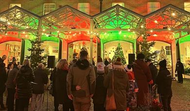 People gather in the Holkham cobbled courtyard singing carols, with red and green lighting.