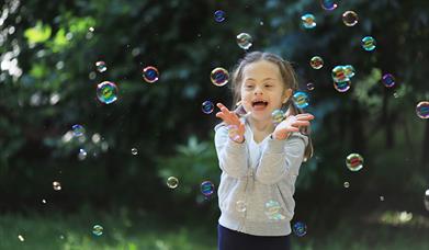 A child plays with giant bubbles in a grassy area.