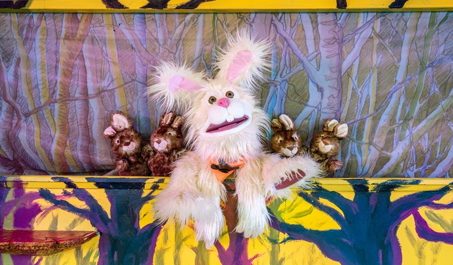 A white fluffy Easter bunny, surrounded by smaller brown bunnies on a stage.