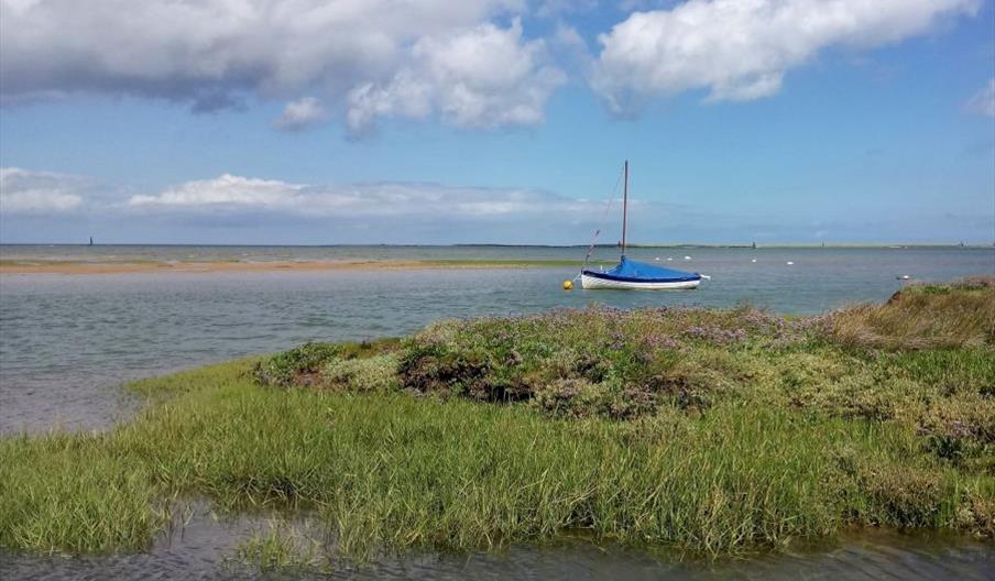 View across saltmarsh at Morston Quay with a boat moored at low tide