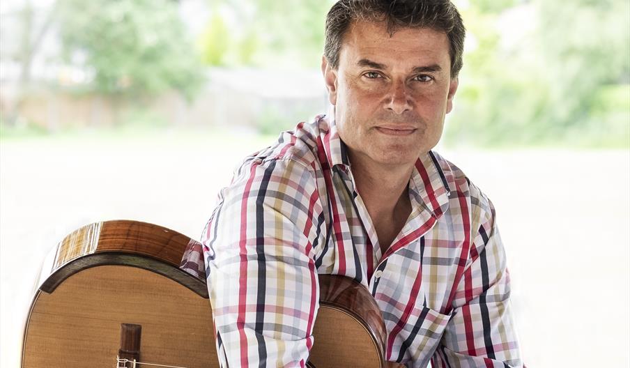 A man casually holds a guitar while looking at the camera.