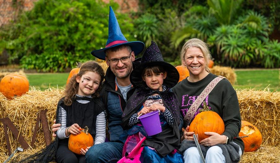 A family dressed in Halloween outfits sit on hay bales at The Halloween Garden at Holkham.