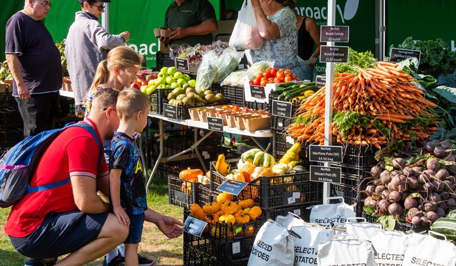 A family browsing the fruit and veg stall at the North Norfolk Food and Drink festival piled high with fresh produce.
