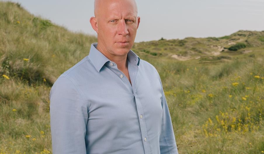 Jake Fiennes stands on the Holkham National Nature Reserve wearing a blue shirt.