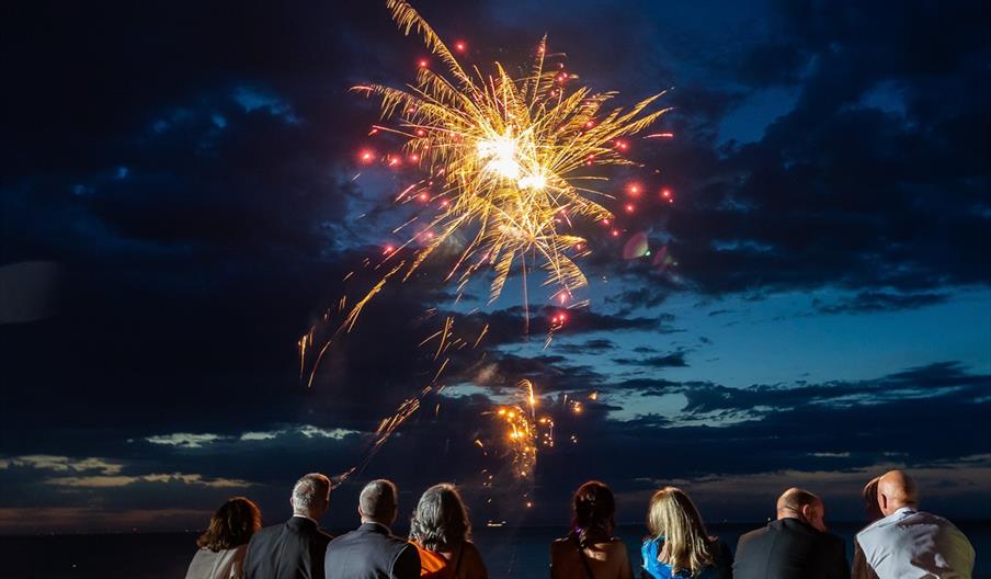 fireworks on the beach with people in black tie watching