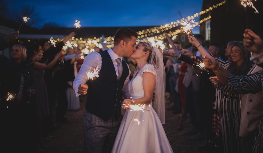 Bride and groom surrounded by guests with sparklers.