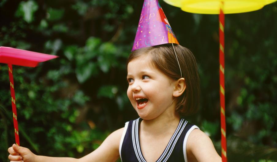 A girl laughs as she is spinning plates and wearing a party hat