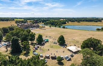 An aerial shot of a collection of food trucks in a semi circle. At Holkham Park. The Hall is situated to the left and the lake is above.