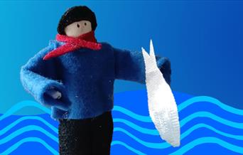 A peg doll dressed in felt clothes asa fisherman with black hat, blue gansey jumper and red necktie, holding a silver fabric fish.