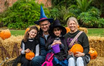 A family dressed in Halloween outfits sit on hay bales at The Halloween Garden at Holkham.